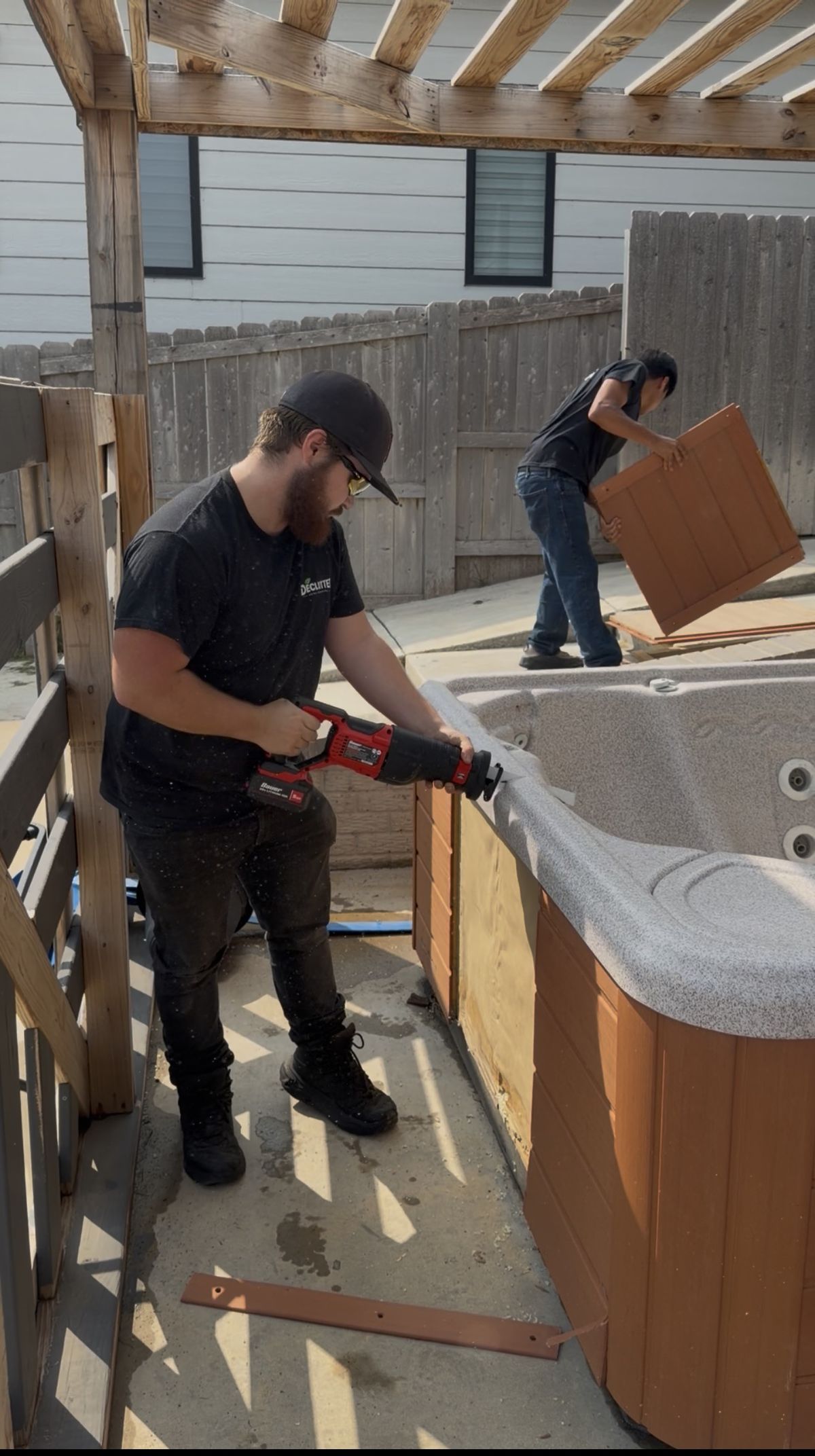 Declutter crew member cutting down an old hot tub under a backyard pergola